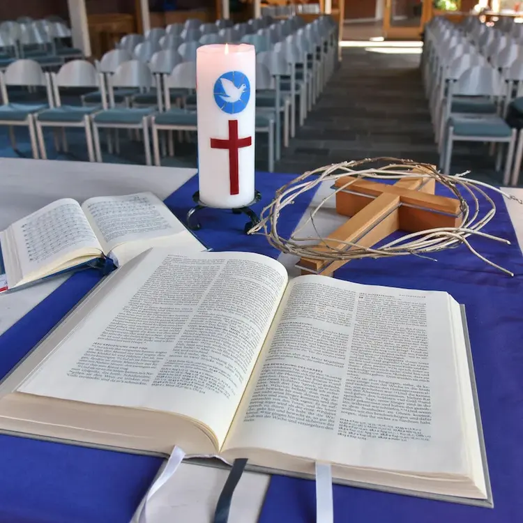 Auf einem Altar liegen aufgeklappt eine Bibel und ein Gesangsbuch, zudem ein Holzkreuz, eine Kerze und ein Weidenring/Dornenkrone.