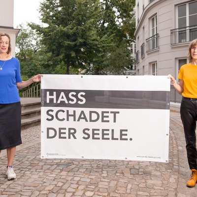 Zwei Frauen halten ein Plakat "Hass schadet der Seele".