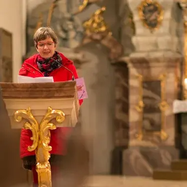 Blick zum Altar. Links ein Lesepult mit Lektorin in roter Jacke