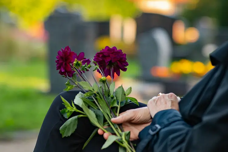 Trauernde auf einem Friedhof mit Blumen.