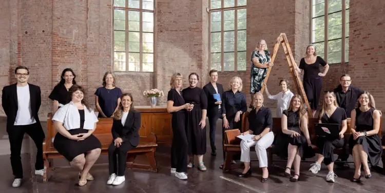 Das Team des Medienreferats stehend und sitzend auf Holzbänken in einer Kirche.